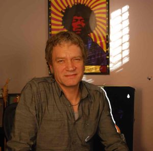 Carl looks at the camera while sitting in front of a Jimi Hendrix show poster.