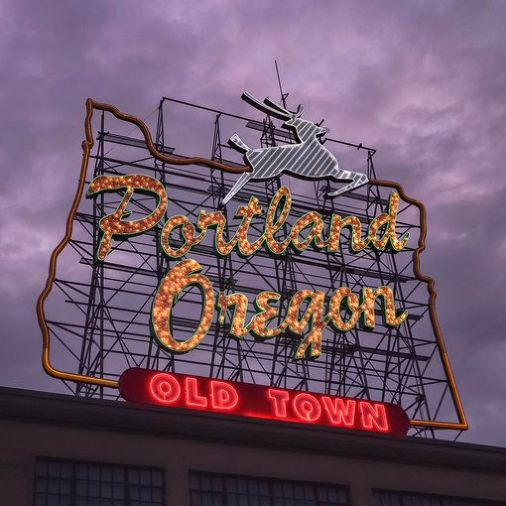 Old Town's light up Portland Oregon sign stands against a cloudy sky in the early dusk.