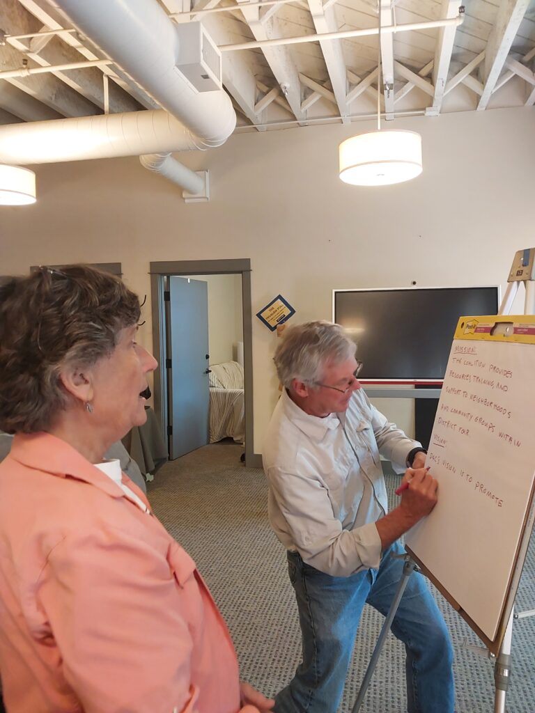 Two board members work on crafting Mission and Vision statements while writing on large paper.