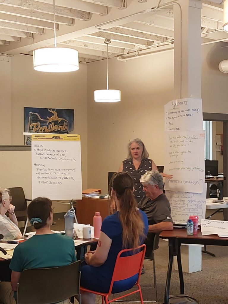 Anna Young speaks to attendees while standing between large sheets of paper containing the event's notes.