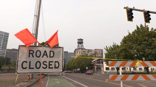 Signs and flags warn that the road is closed near the old Centennial Mills warehouse, which caught fire in August 2026.