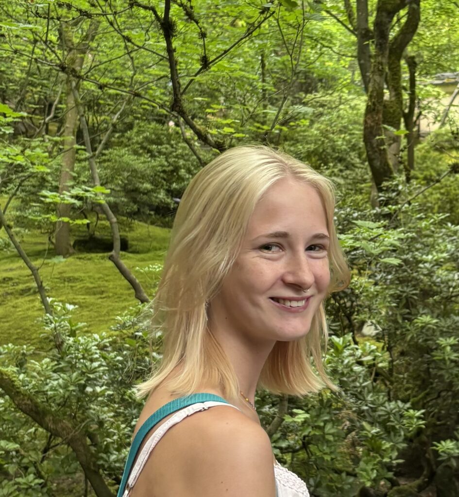 A headshot of a woman smiles at the camera with a background of trees.