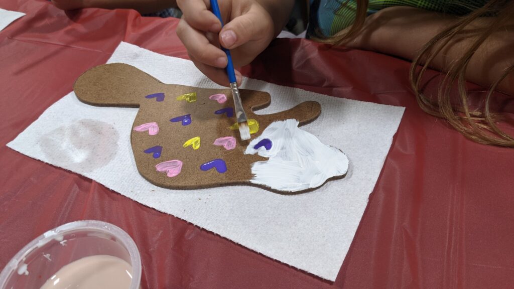 A child paints a wooden beaver cutout with colorful hearts